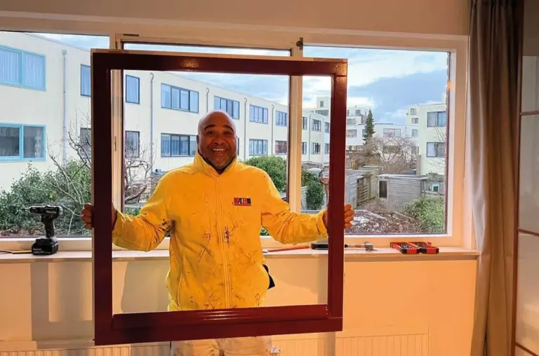 A professional holding a newly removed dark wooden window frame in front of a large residential window during a window replacement project.